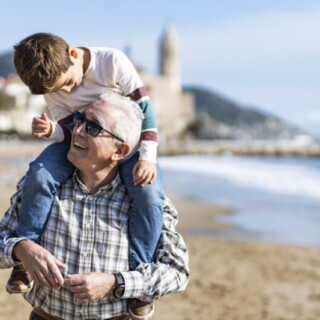 Older person at the beach with a a younger person on his shoulders