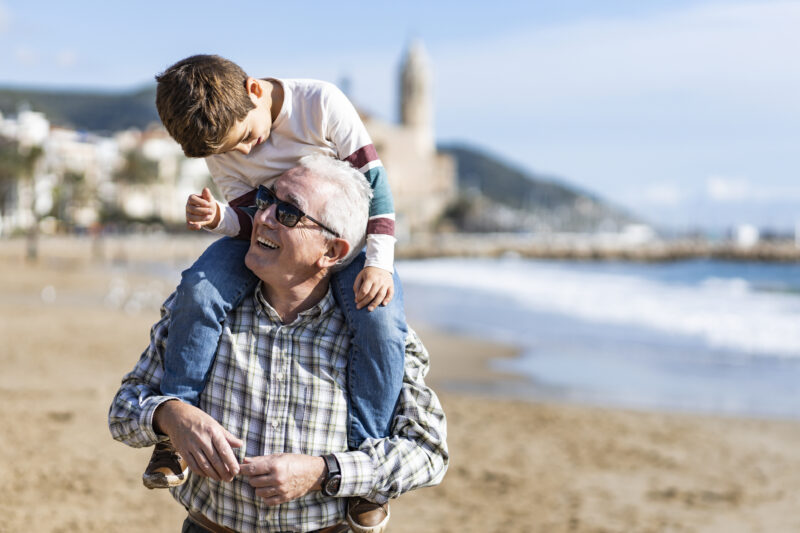 Older person at the beach with a a younger person on his shoulders